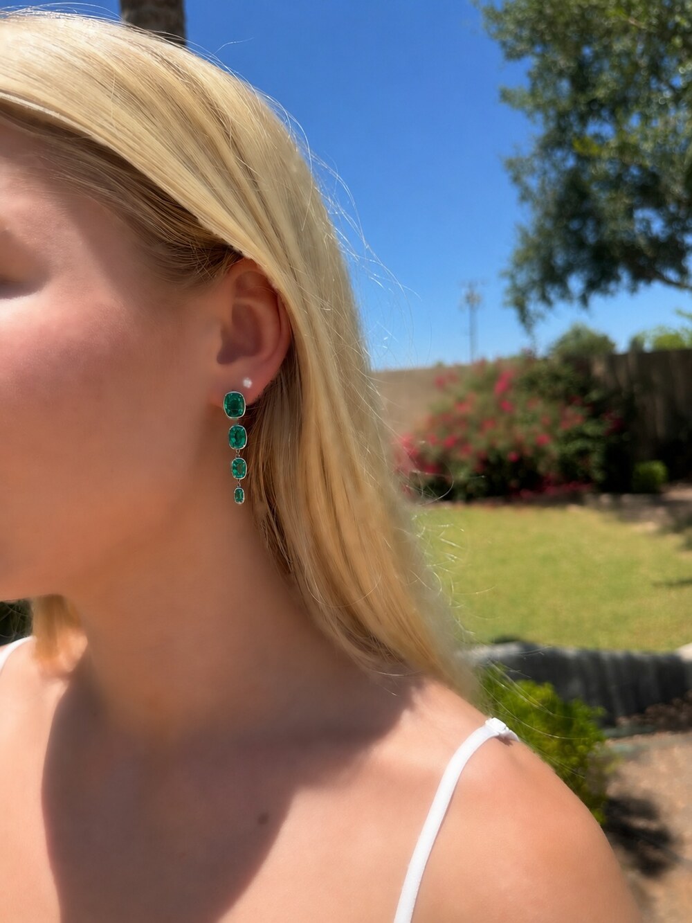 The Columbian Rain drop earrings worn on the ear — a vertical cascade of four bezel-set rectangular cushion-cut lab-grown emeralds in platinum, shown as a pair