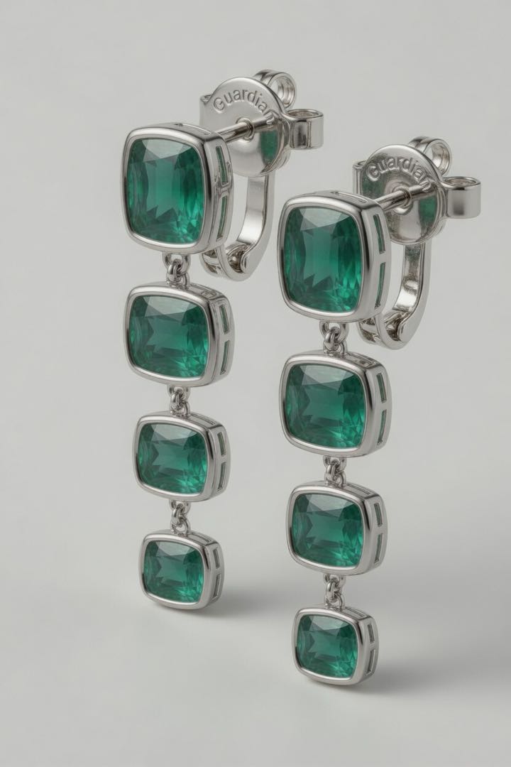 Pair of platinum cascading drop earrings — four graduated bezel-set lab-grown emeralds in deep forest green descend vertically from the stud, with the Guardian-engraved locking earring back clearly visible behind the top stone.